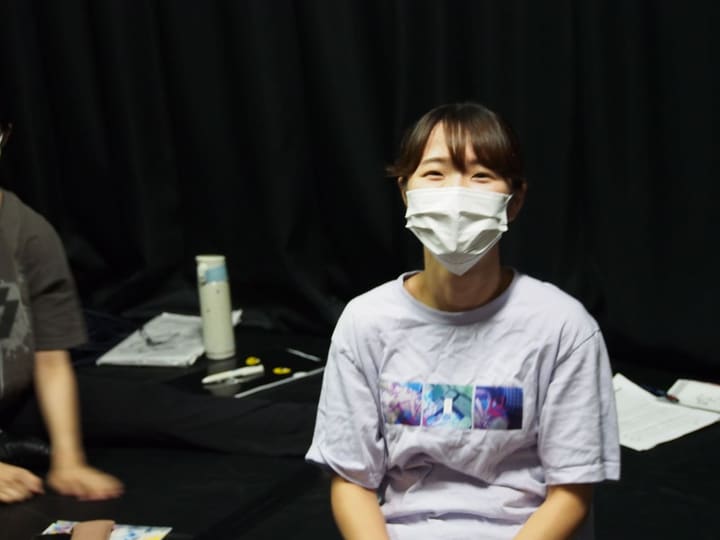 黒い稽古場で腰かけ、笑顔でカメラを見る団員｜劇団カスタリア 稽古オフショット