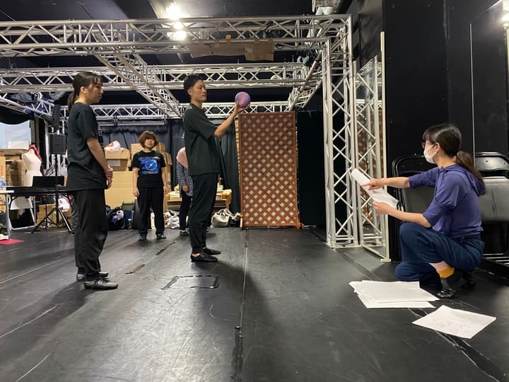 紙を手に膝をついた指導役が、ボールを持つ出演者に段取りを伝える｜劇団カスタリア「TRIP」立ち稽古