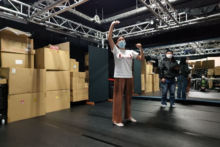 片腕を高く上げたポーズで立つ団員と、後方で見守る講師｜劇団カスタリア 演技稽古