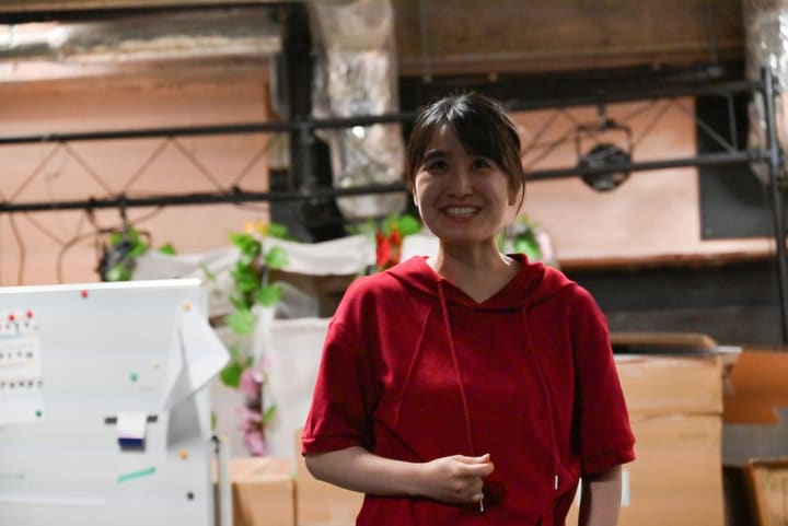 赤いパーカー姿で笑顔を見せる団員、左奥にホワイトボード|劇団カスタリア「ルドベキアフェスティバル」稽古