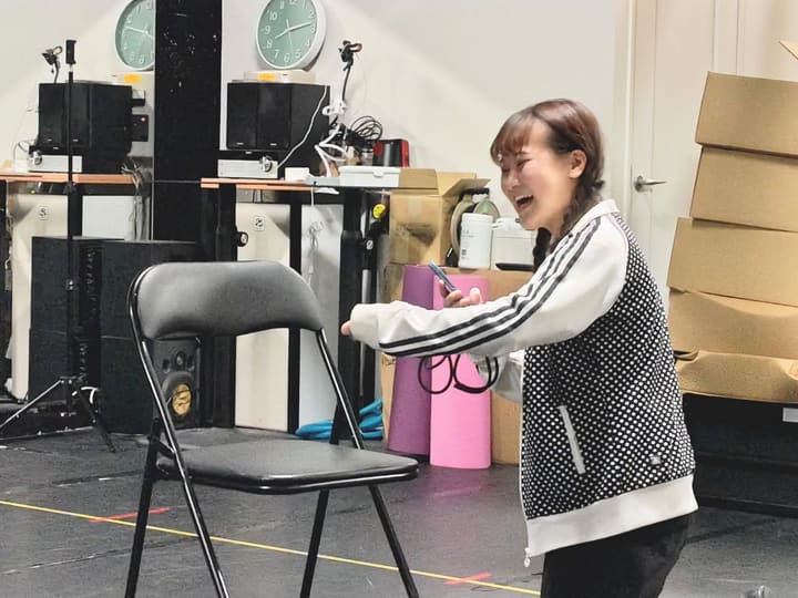 パイプ椅子の前で口を大きく開けて笑う場面を演じる団員|劇団カスタリア 演技稽古
