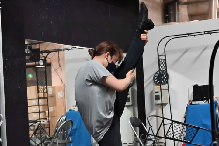 脚を垂直近くまで上げて柱に寄り体を伸ばす団員｜劇団カスタリア 稽古前のストレッチ