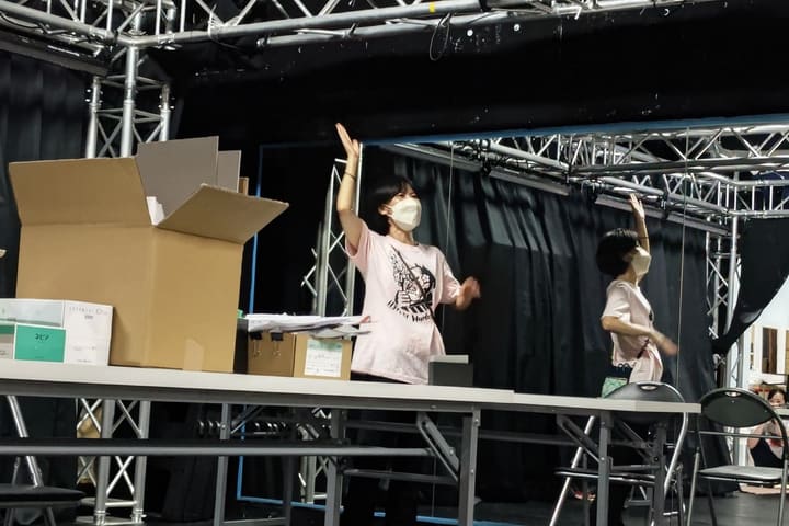 長机の奥で片腕を高く上げる動きをそろえる出演者2人｜劇団カスタリア 二人芝居の稽古