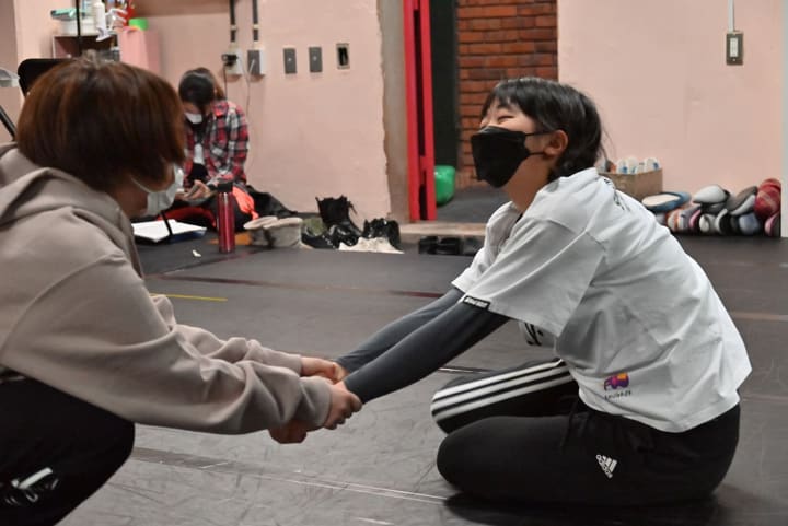 床に座った団員が仲間に腕を引かれ、笑いながら体を伸ばすストレッチ｜劇団カスタリア 稽古前のストレッチ