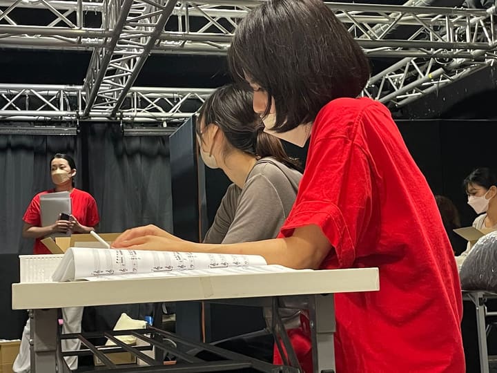 キーボードの譜面台に広げた楽譜を覗き込む団員2人|劇団カスタリア 歌稽古