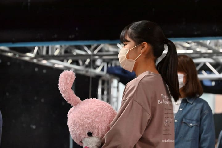 ピンクのぬいぐるみを抱えたまま、次の場面を待つ団員の横顔|劇団カスタリア ナンバー稽古