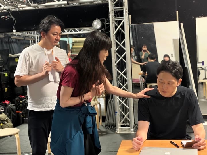 机に向かう公に、そっと肩へ手を伸ばす芝居を確かめる出演者たち｜劇団カスタリア 芝居稽古