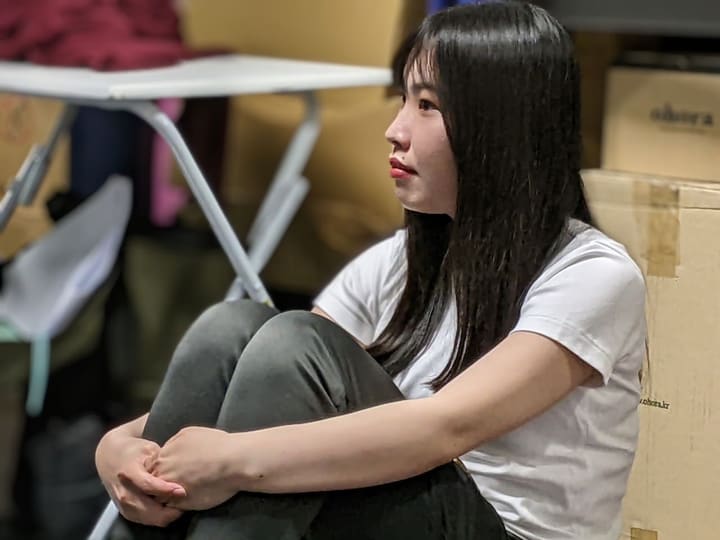 膝を抱えて床に座り、じっと前を見つめる出演者|劇団カスタリア「TRIP」立ち稽古