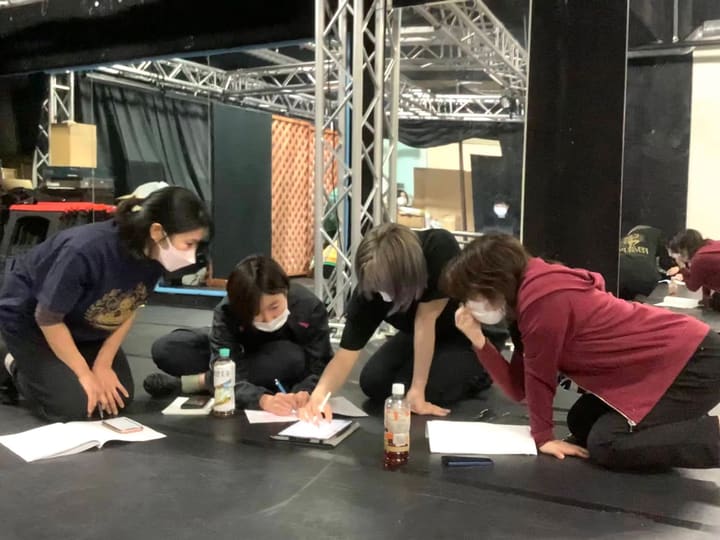 床に広げた紙をのぞき込み、書き込みを加える団員4人｜劇団カスタリア「ルドベキアフェスティバル」本読み