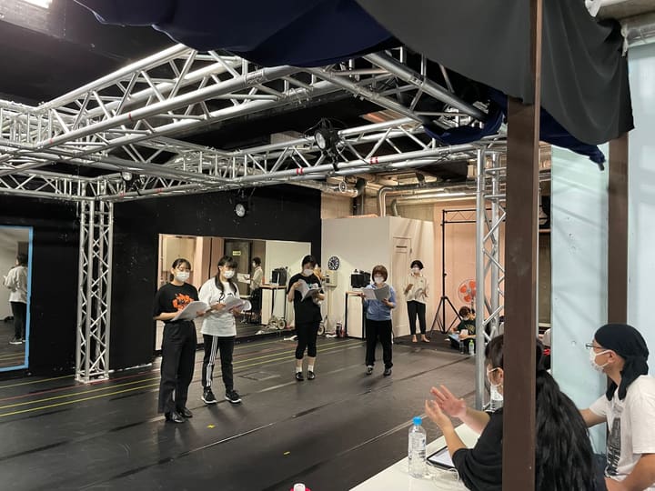 台本を手に並んだ団員へ、机の側から指示が飛ぶ稽古場｜劇団カスタリア 立ち稽古