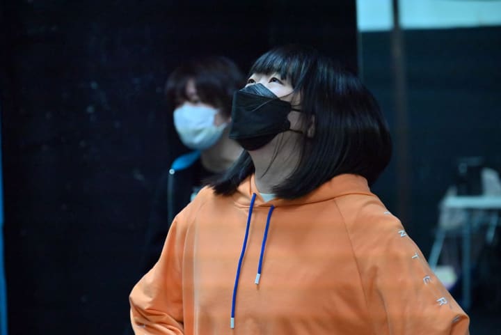 オレンジのパーカー姿で顔を上げ、視線を上へ向ける出演者|劇団カスタリア お芝居の稽古