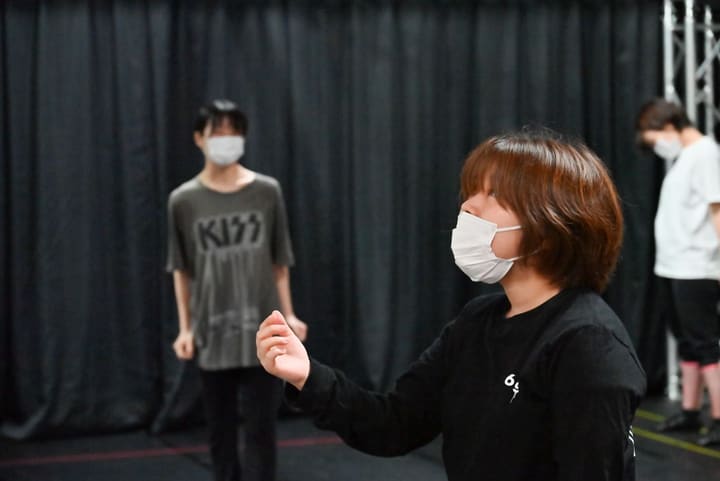 胸の前で手を軽く丸め、顔を上げて演じる団員と奥に立つ出演者2人｜劇団カスタリア 稽古