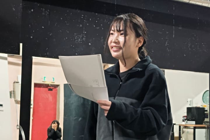 プリントを手に笑顔で声を出す団員と、奥で見守る仲間|劇団カスタリア 歌レッスン