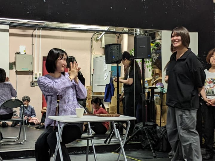 机に着いた役が手を合わせて喜び、隣で笑って見守る出演者｜劇団カスタリア「TRIP」立ち稽古
