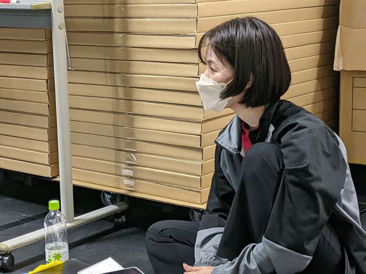 段ボールの脇に腰を下ろし、芝居の稽古を見つめる団員｜劇団カスタリア 演技稽古