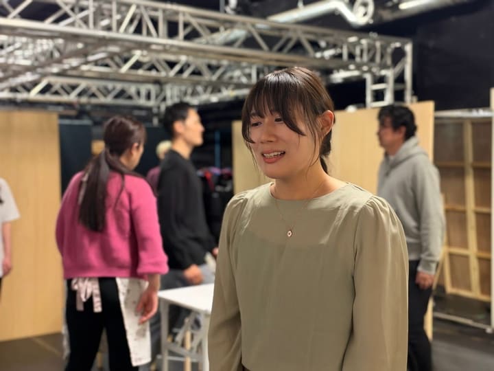 稽古場でほほえむ出演者。奥では別の団員が立ち話をしている|劇団カスタリア 稽古場