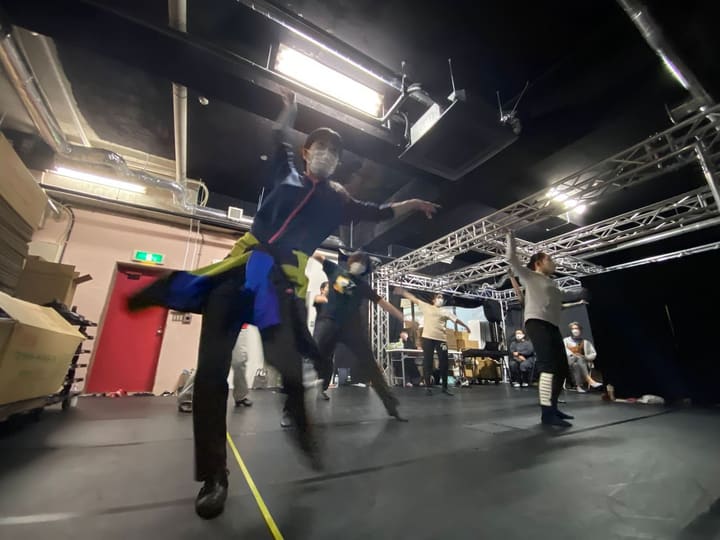 片脚を高く上げ腕を広げて踊る団員と、見守る仲間たち｜劇団カスタリア ダンス稽古