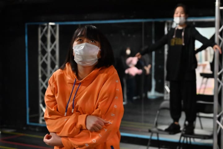 オレンジのパーカーで腕を抱え、上を見上げる団員｜劇団カスタリア ステージング稽古