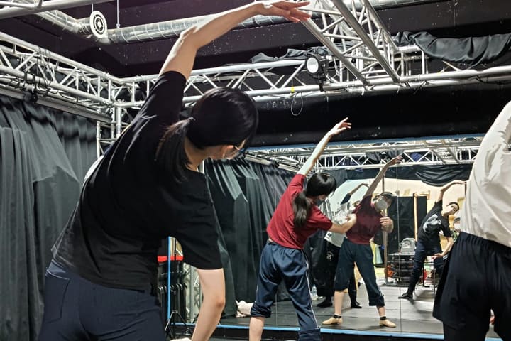 片腕を頭上へ伸ばして体側を倒し、柔軟を行う団員たち｜劇団カスタリア ダンス稽古