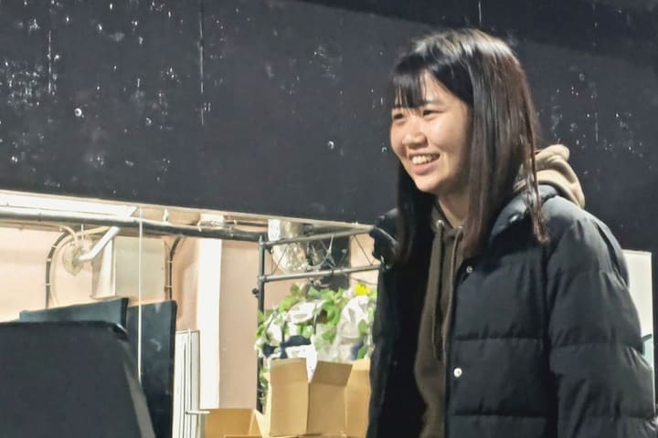 厚手のジャケット姿で、笑顔で稽古を見つめる団員|劇団カスタリア 歌稽古