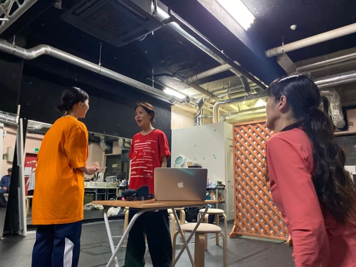 机をはさんで立ち、台詞を交わす3人の出演者｜劇団カスタリア 芝居稽古