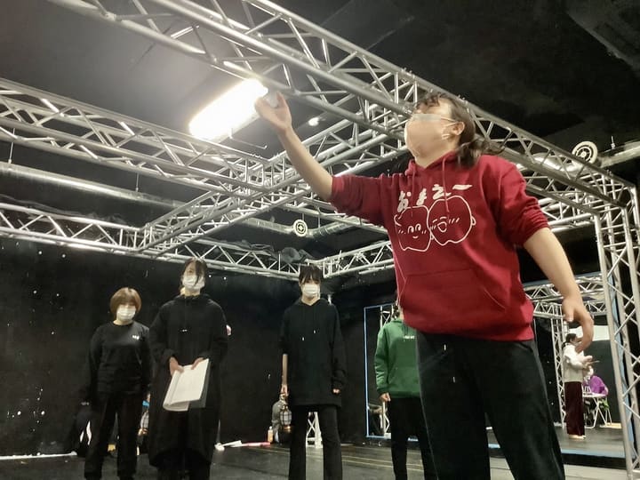 片手を高く掲げて空を仰ぐ演技を、台本を持つ仲間が見守る｜劇団カスタリア 通し稽古