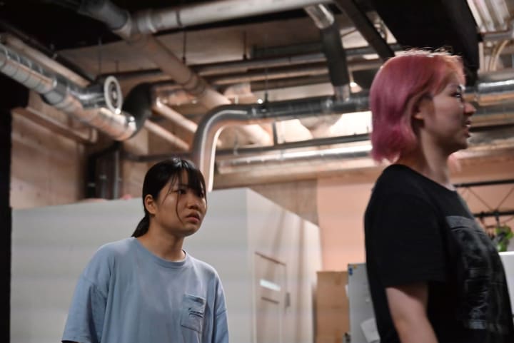 ピンク髪の出演者の背後で、硬い表情を見せる出演者｜劇団カスタリア 通し稽古