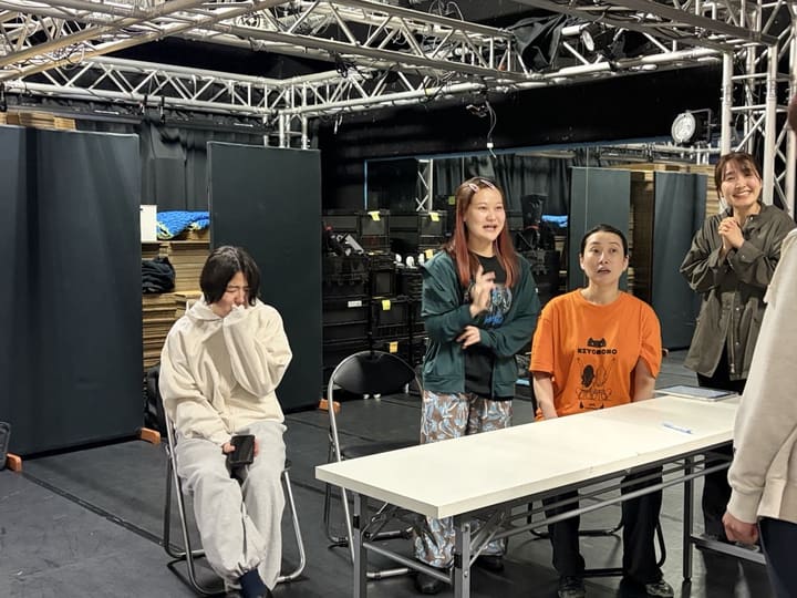 長机を囲む場面を、笑いながら演じる出演者たち｜劇団カスタリア「金曜日の食卓」立ち稽古