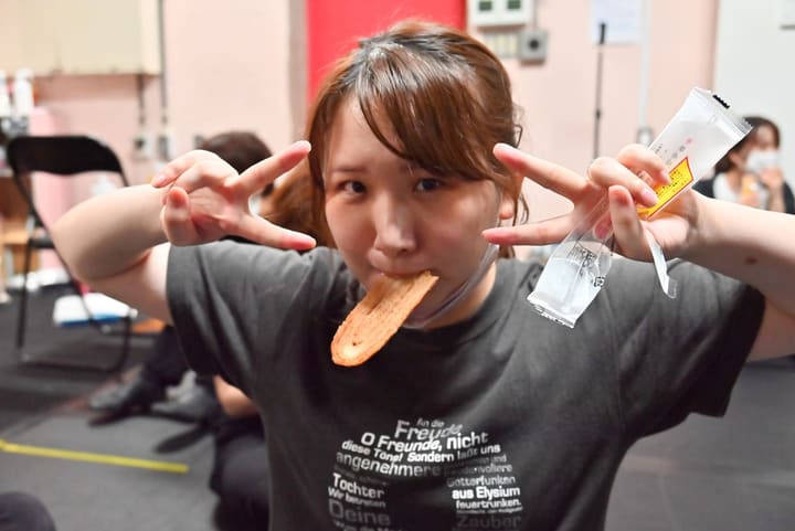 差し入れのお菓子をくわえ、両手でピースサインを作る団員|劇団カスタリア 稽古オフショット