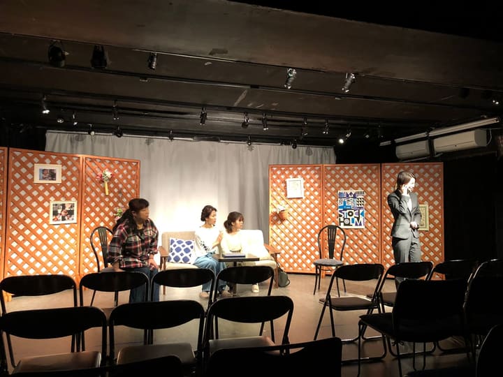 居間のセットで語り合う3人と、離れて電話をする人物の芝居|劇団カスタリア「DAHLIA」公演