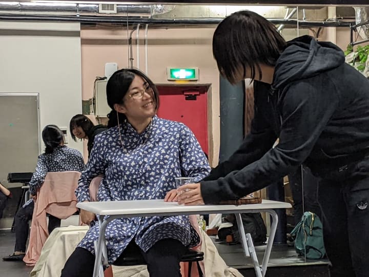 机にグラスを置く相手役と、椅子に腰かけて笑う出演者｜劇団カスタリア 抜き稽古