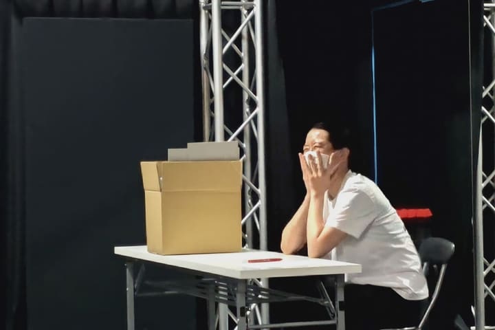 机に着き、両手を顔に当てて感情を表す出演者｜劇団カスタリア 演技稽古