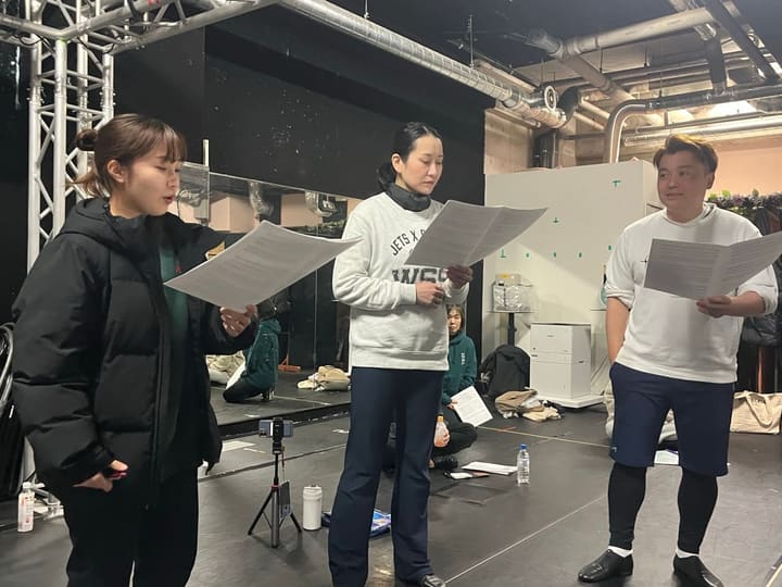 譜面を手に横一列で歌う団員3人と、三脚のスマートフォンで記録する稽古場|劇団カスタリア 歌稽古