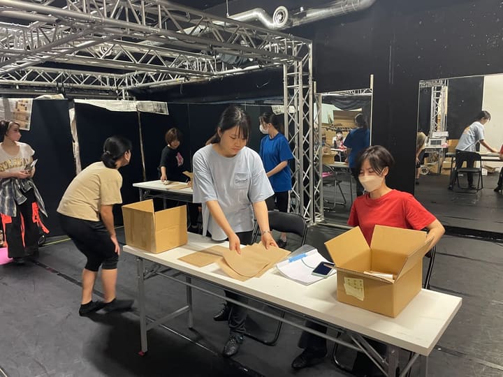 長机に段ボール箱を並べ、紙を手に取る出演者たち｜劇団カスタリア 通し稽古