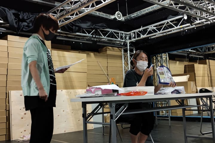 机の品物を手に取る出演者と、台本を手に立つ出演者｜劇団カスタリア 演技稽古