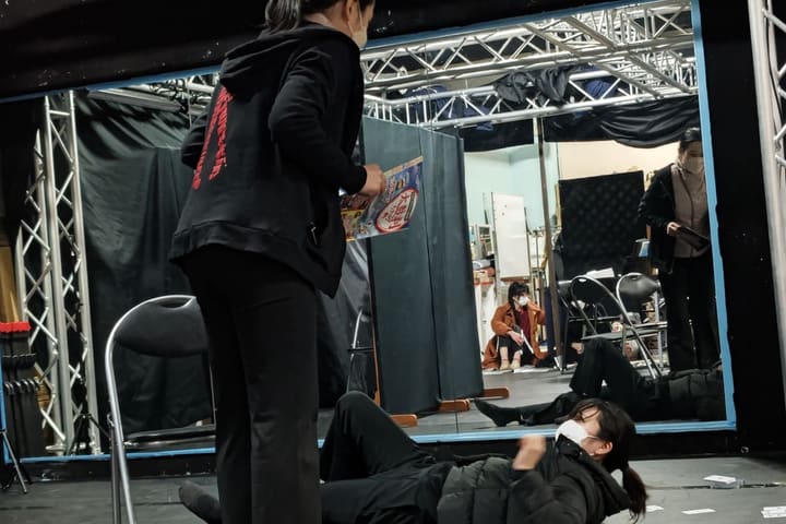 冊子を手に立つ団員と、床に寝転がる団員の二人芝居|劇団カスタリア 演技稽古