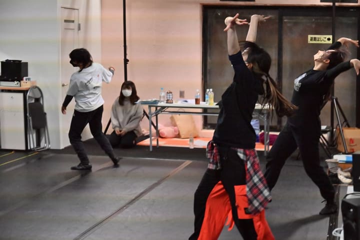 両腕を頭上に伸ばし上体を反らせて踊る団員たちと、床で見守る仲間｜劇団カスタリア ダンス稽古