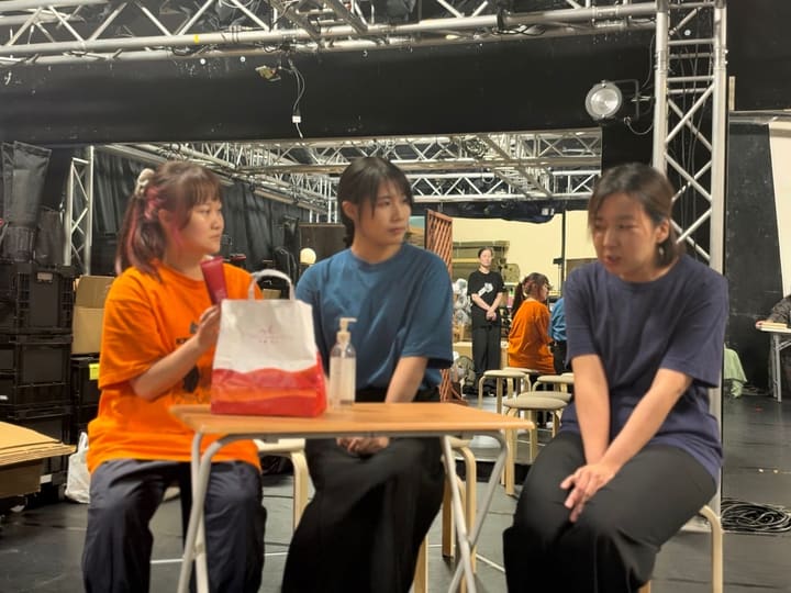 机を囲んで腰かけ、芝居の段取りを確かめる3人の出演者｜劇団カスタリア 芝居稽古