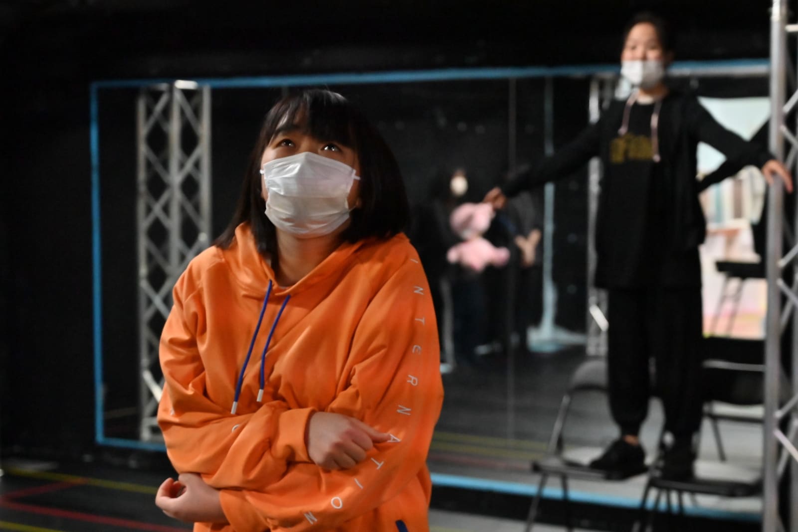 オレンジのパーカーで腕を抱え、上を見上げる団員|劇団カスタリア ステージング稽古