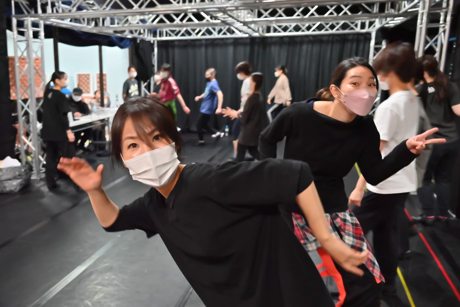 大勢が踊る稽古場の手前で、カメラに向かってポーズをとる2人|劇団カスタリア 稽古オフショット
