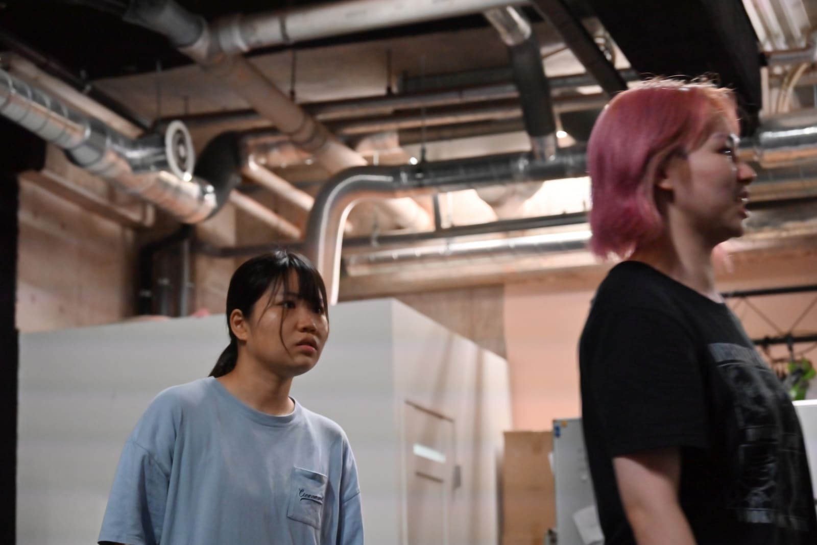 ピンク髪の出演者の背後で、硬い表情を見せる出演者|劇団カスタリア 通し稽古