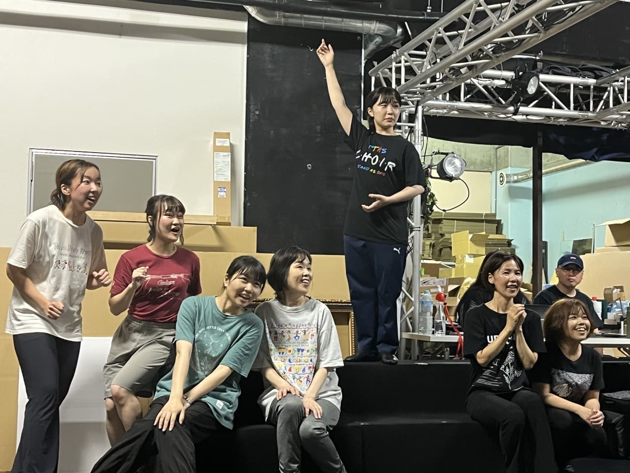 台の上から腕を高く上げて歌う出演者と、笑顔で見守る仲間たち|劇団カスタリア「清子と桃香」稽古