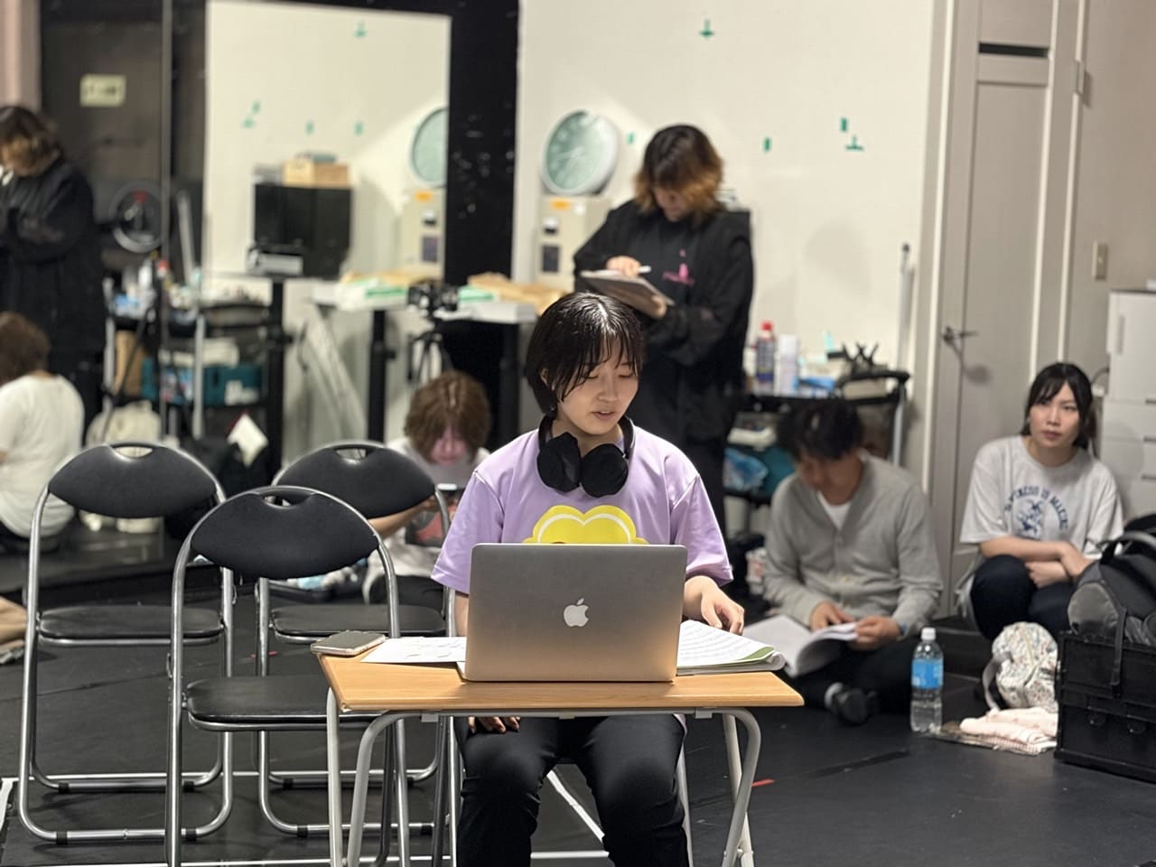 稽古場の机でノートパソコンに向かい制作作業を進める団員と、床で台本を読み込むメンバー｜劇団カスタリア「金曜日の食卓」稽古